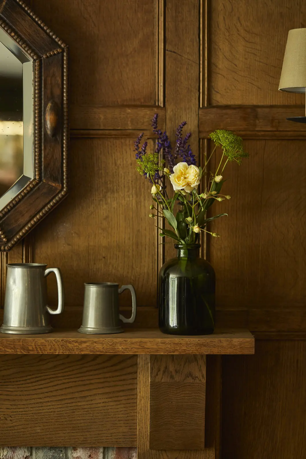 Wild flowers in a green glass vase by pewter tankards
